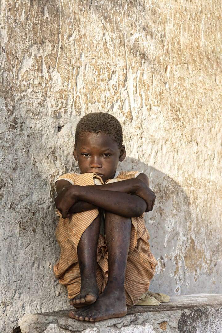 A young boy sitting against the wall with his arms crossed.