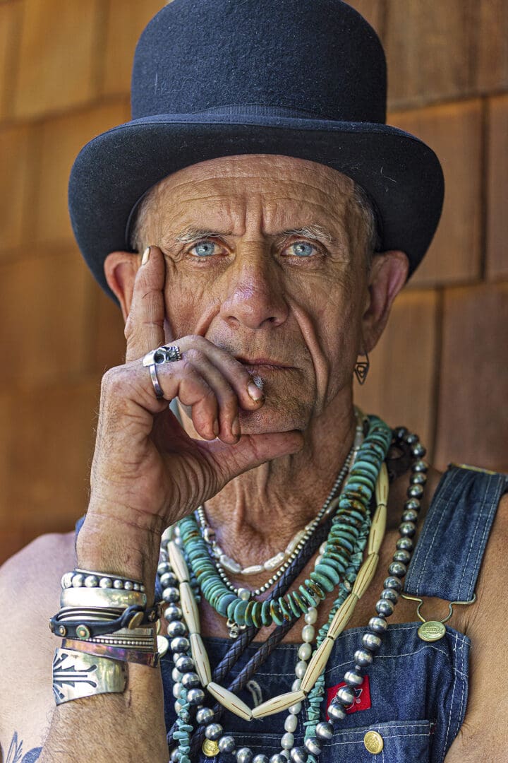 A man with blue eyes and black hat smoking.