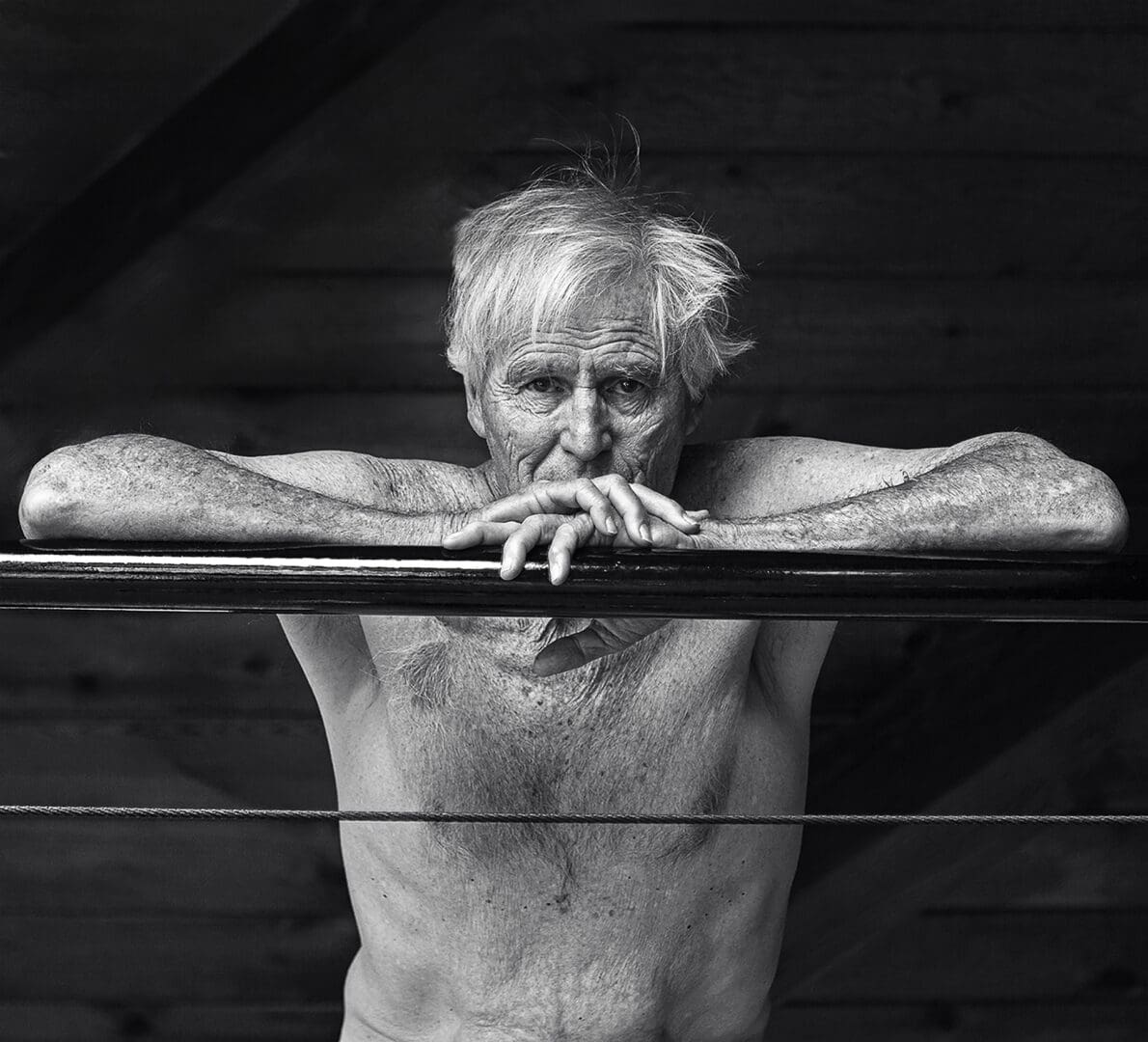 A shirtless man leaning on the railing of a metal fence.