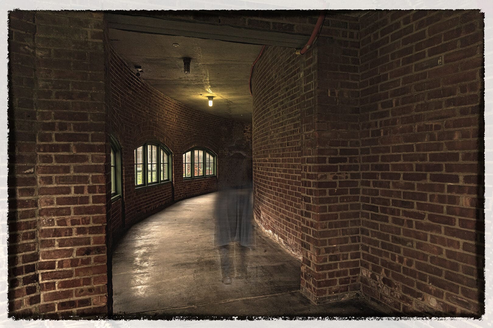 A person is walking in the dark through an old brick hallway.