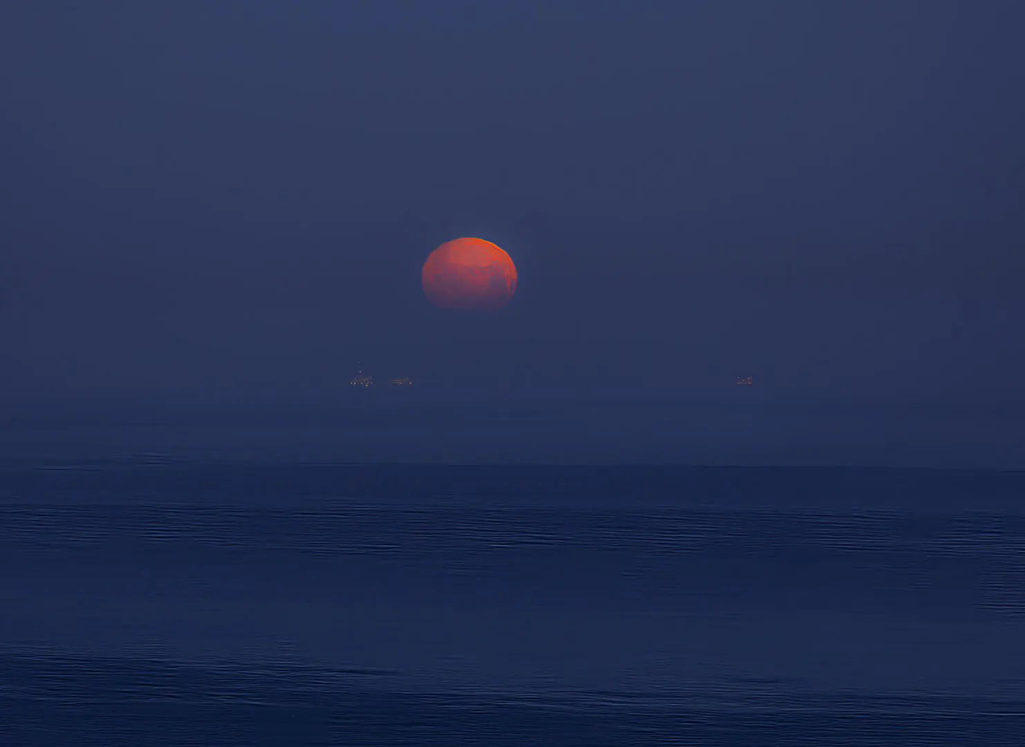 A red moon setting over the ocean at dusk.