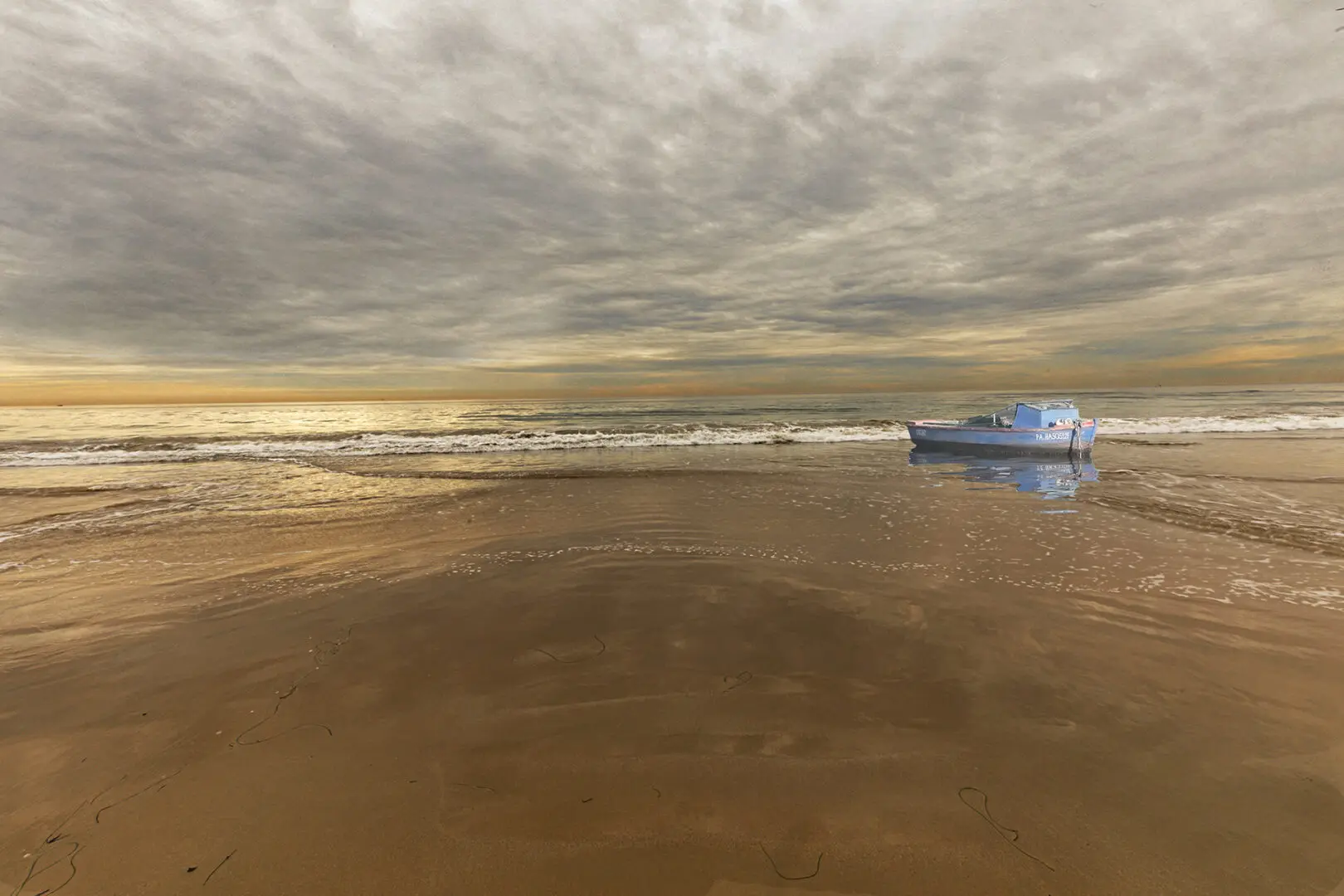 A boat is sitting on the beach at sunset.