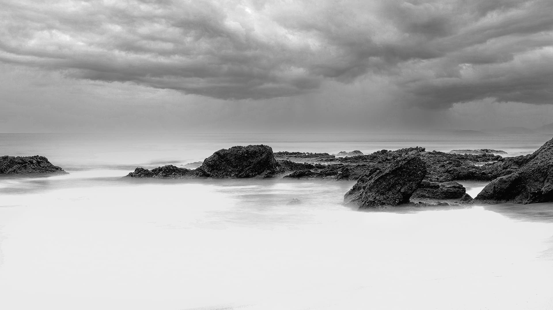 Black and white rocky shoreline with storm clouds